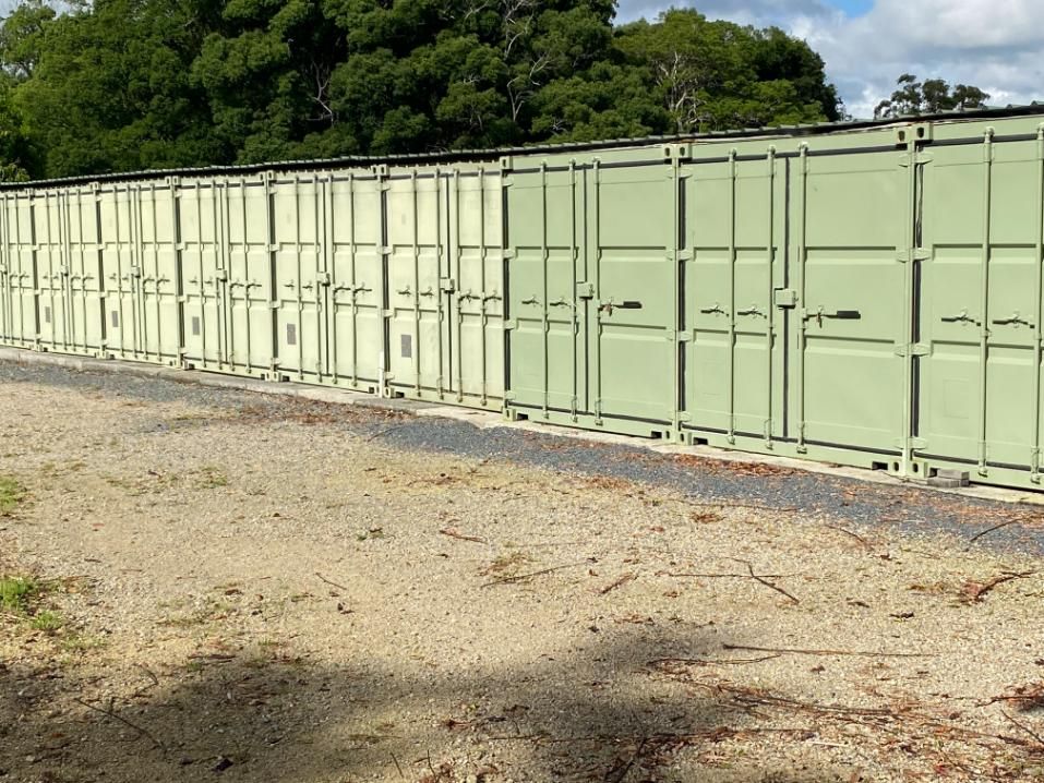 A Row Of Green Shipping Containers Are Lined Up Next To Each Other In A Dirt Field — Byron Storage Services In Myocum, NSW