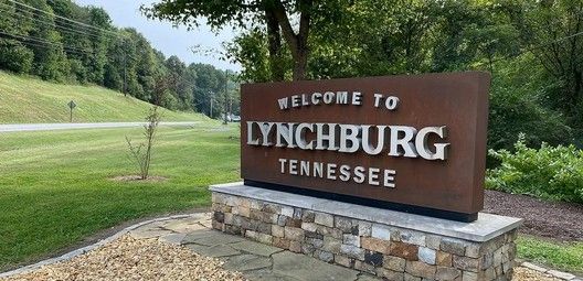 Sign welcoming visitors to Lynchburg, Tennessee. The sign is brown with silver lettering, set on a stone base.