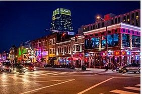 Nighttime street scene in Nashville, Tennessee, with brightly lit bars and buildings lining the road.