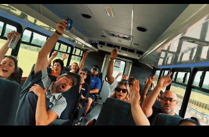 A woman and a man high-five in front of a bus, smiling. Several people board the bus.