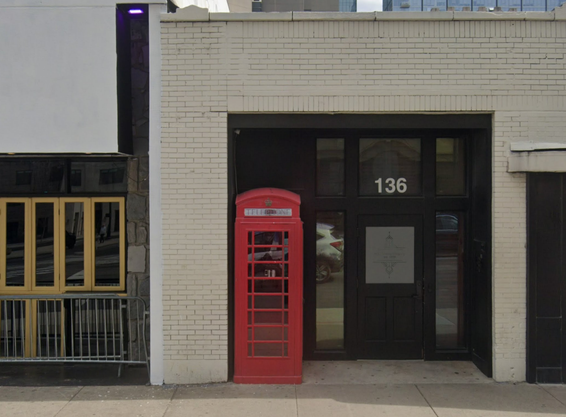 Red phone booth in front of a building with the number 136 on the door. The building has a white brick exterior.