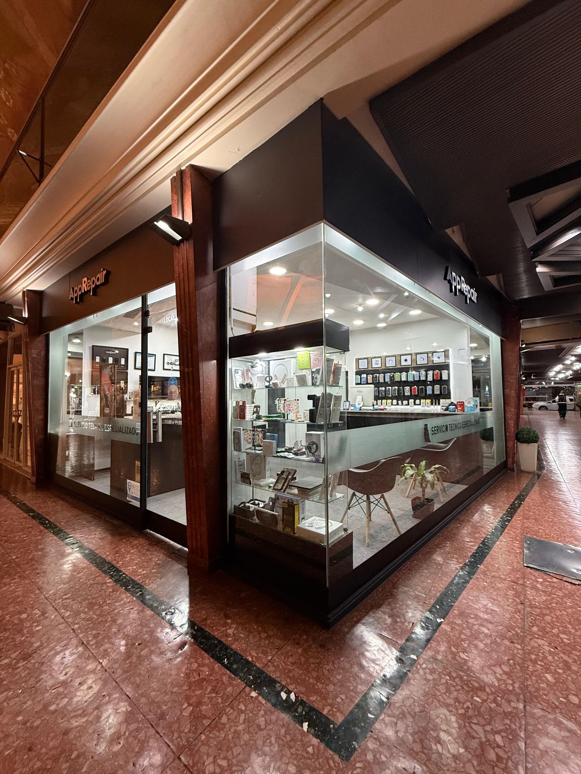 Una tienda con grandes ventanales en un centro comercial con suelo de baldosas rojas. En el interior se exhiben productos.