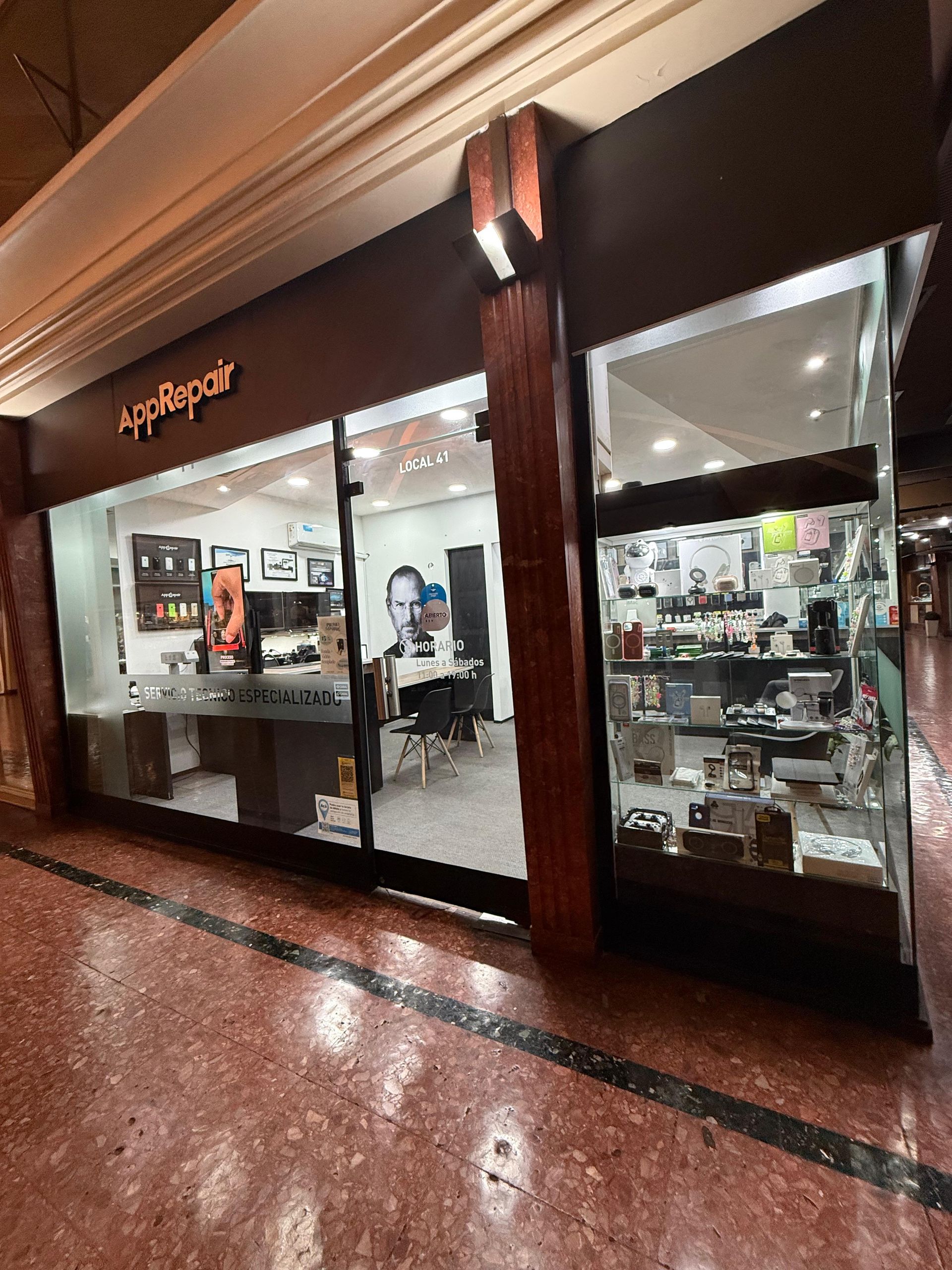 Exterior de una tienda iRepair con ventanas de cristal, detalles en marrón y mercancía expuesta.