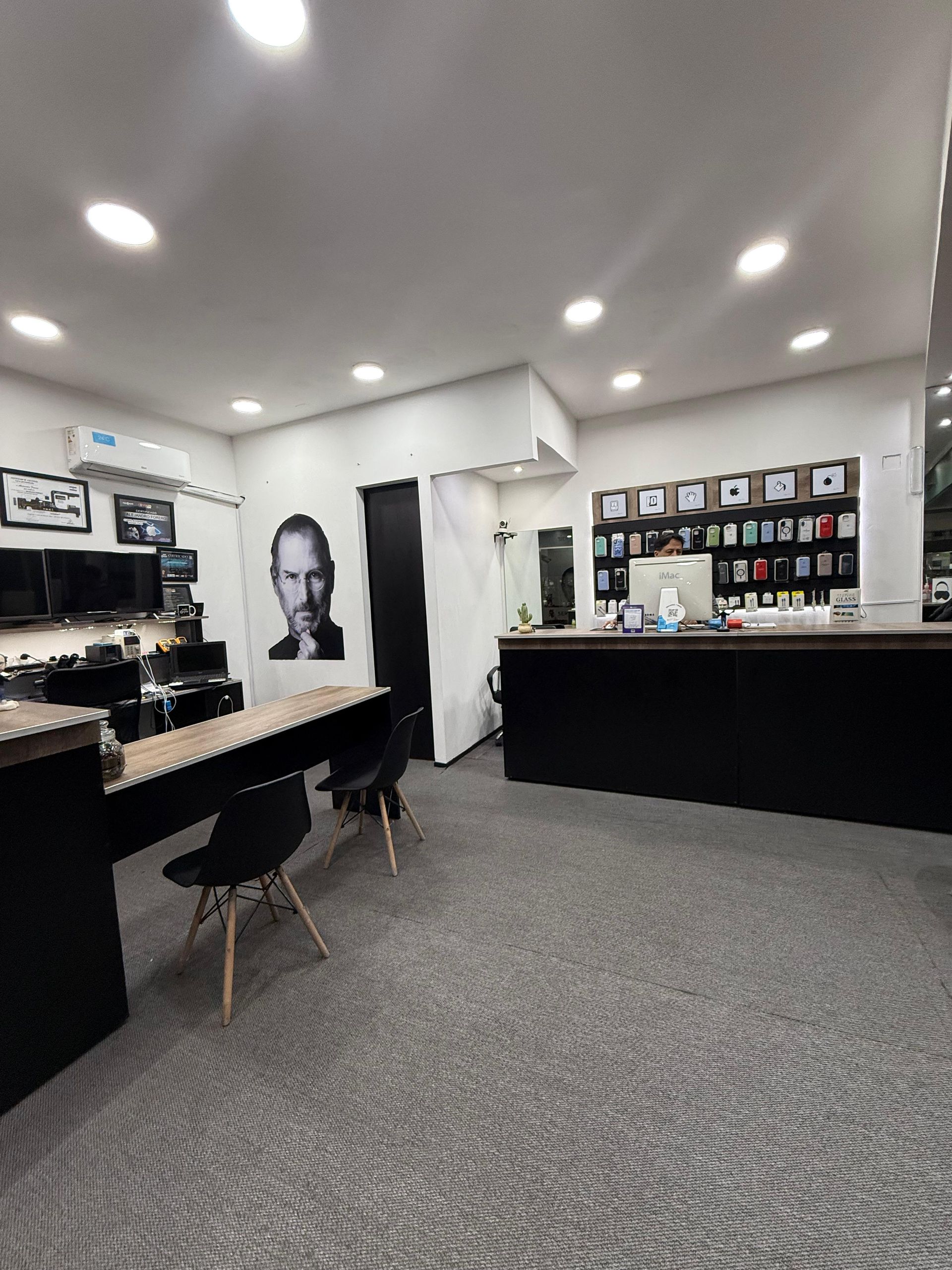 Interior de una tienda de electrónica con un gran retrato de Steve Jobs, mostradores oscuros y productos en exhibición.