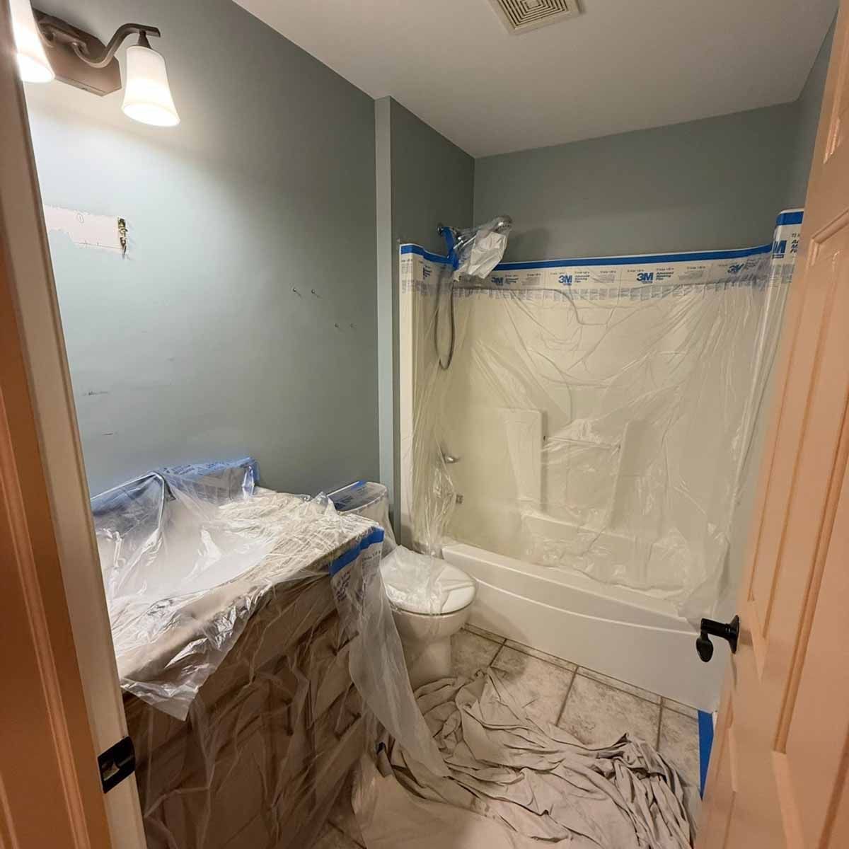 Bathroom with blue-gray walls, white fixtures, and plastic covering during renovation.