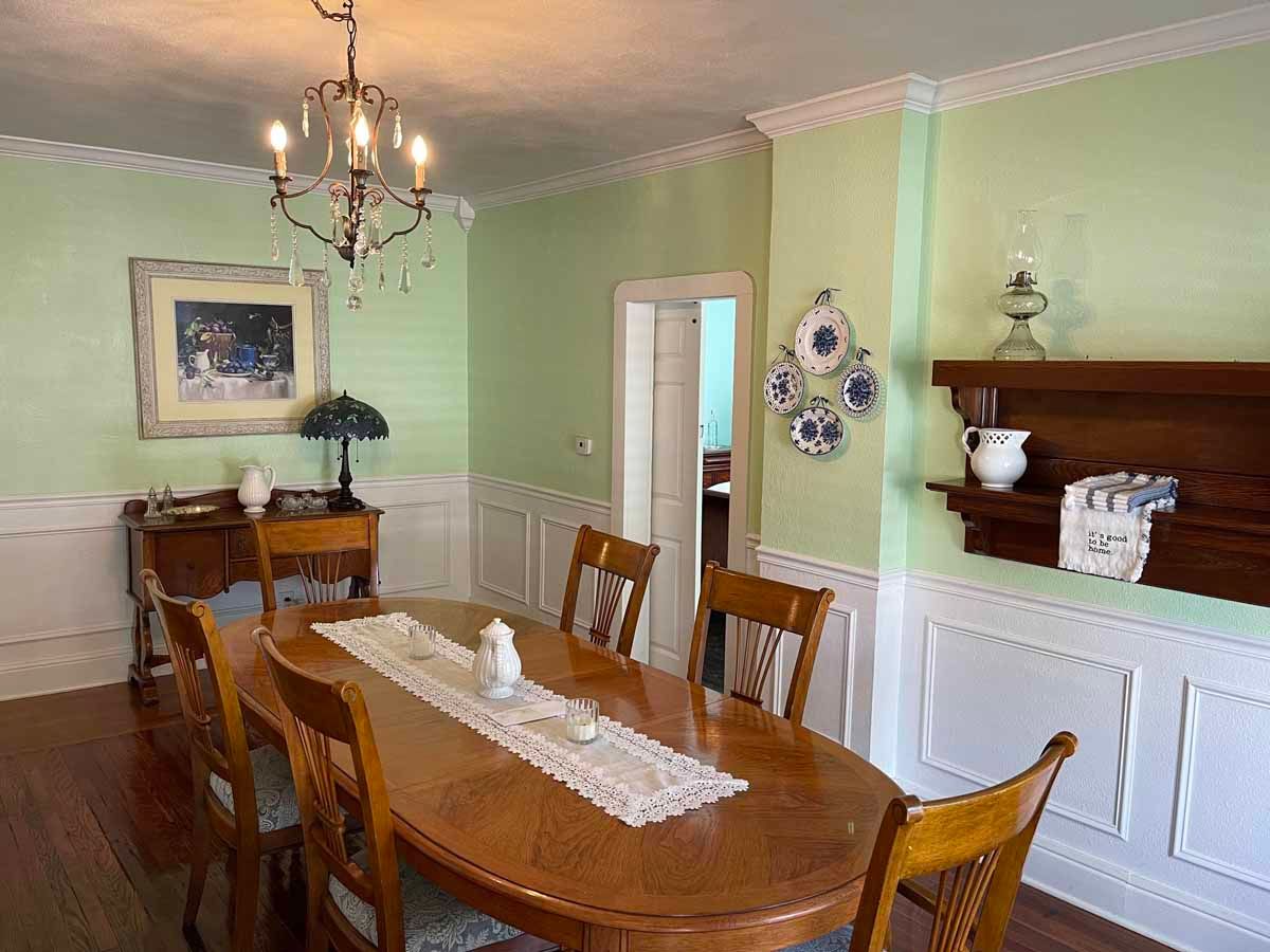 Dining room with wooden table and chairs, light green walls, and a chandelier.