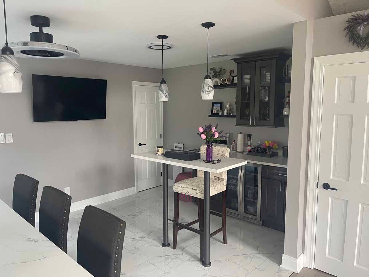 A kitchen/bar area featuring a countertop, bar stools, a TV, and a cabinet with liquor.