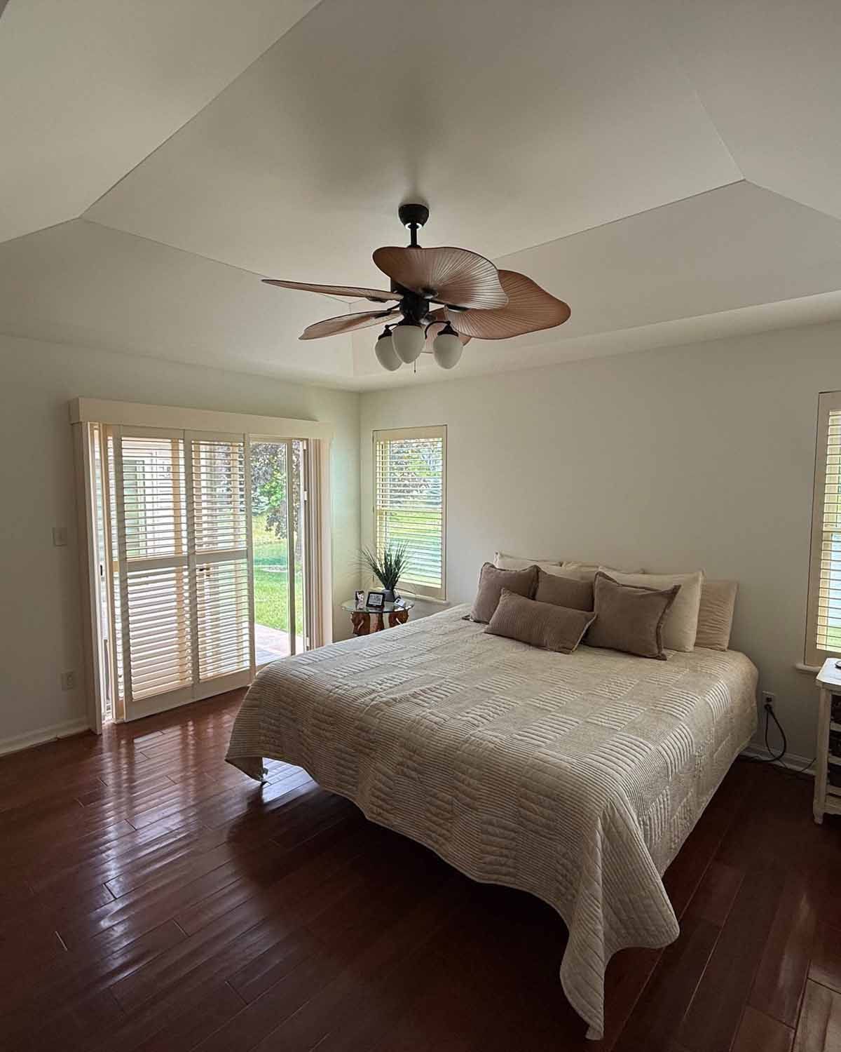 Bedroom with hardwood floors, bed, and ceiling fan; sliding door to a green view.