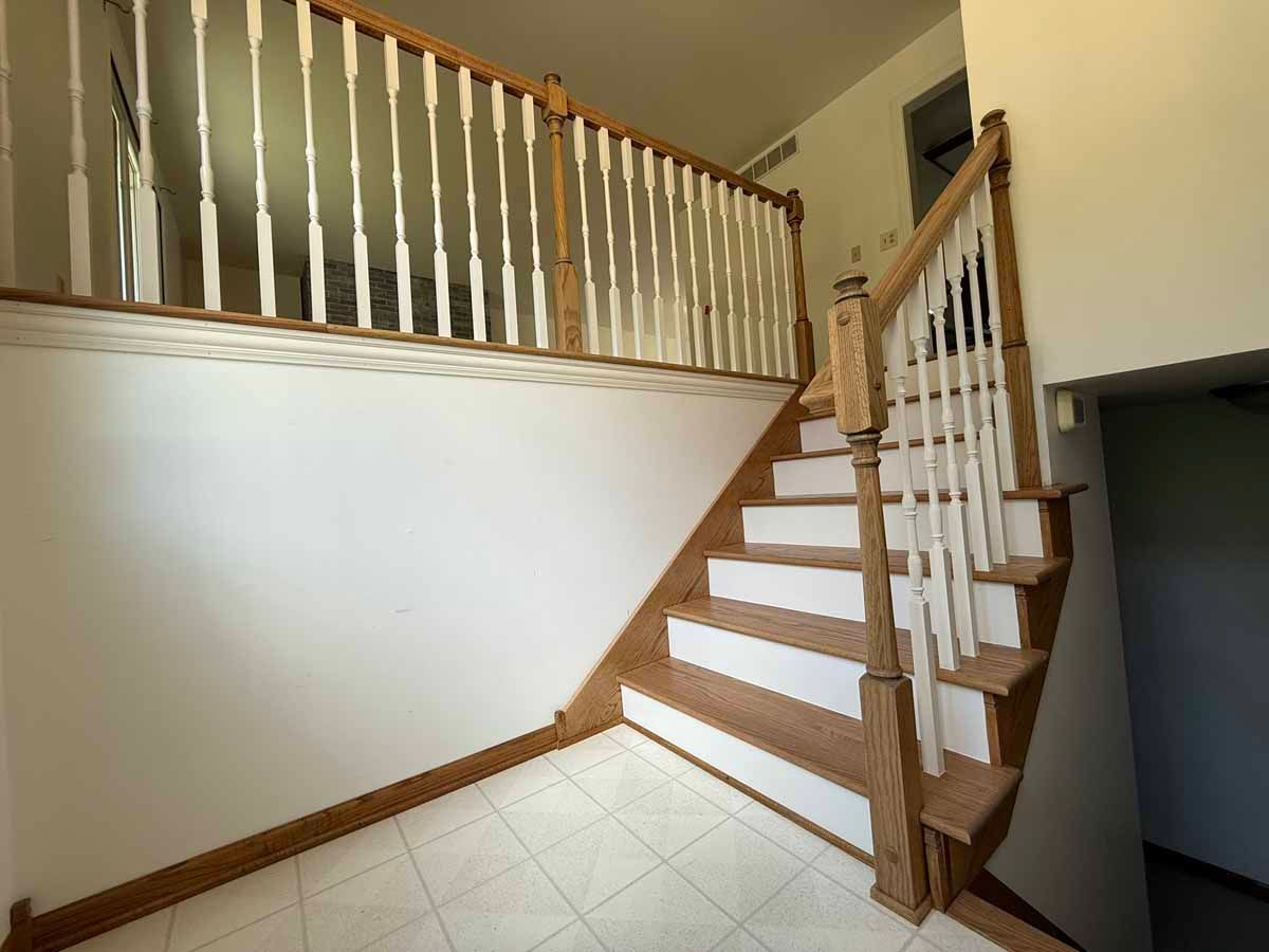 Staircase with white and wood railings leading to a second level. Entryway with tiled floor and white walls.