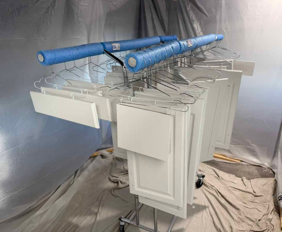 White cabinet doors hanging on wire racks with blue pool noodles, in a makeshift paint booth.