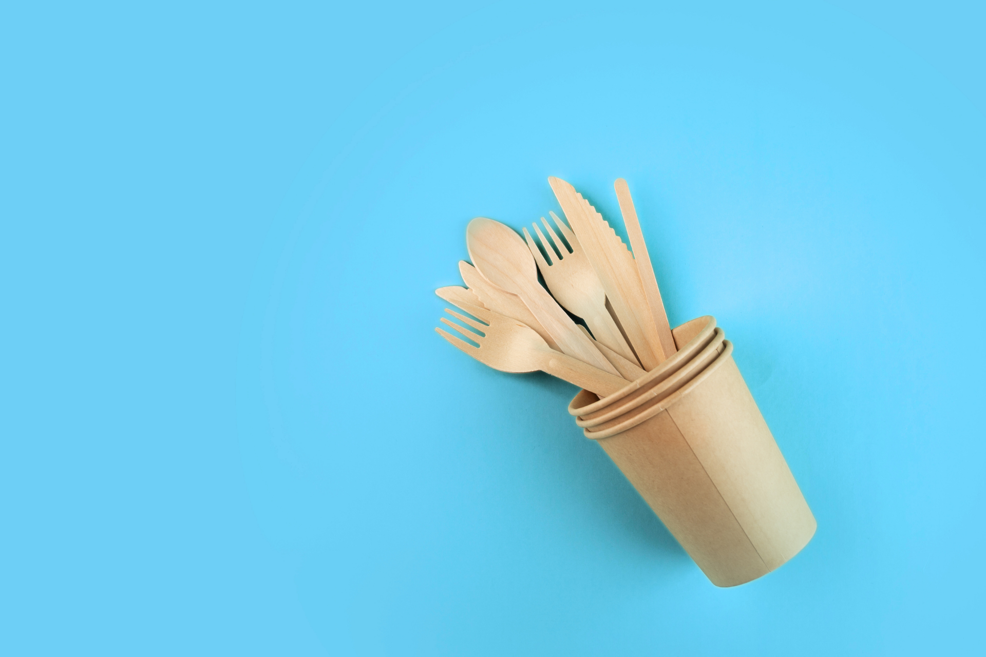 A stack of paper cups filled with wooden utensils on a blue background.