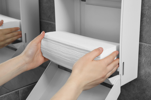 A person is taking a roll of paper towels out of a paper towel dispenser.