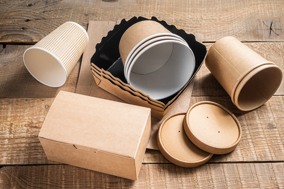 A wooden table topped with paper cups , boxes and lids.