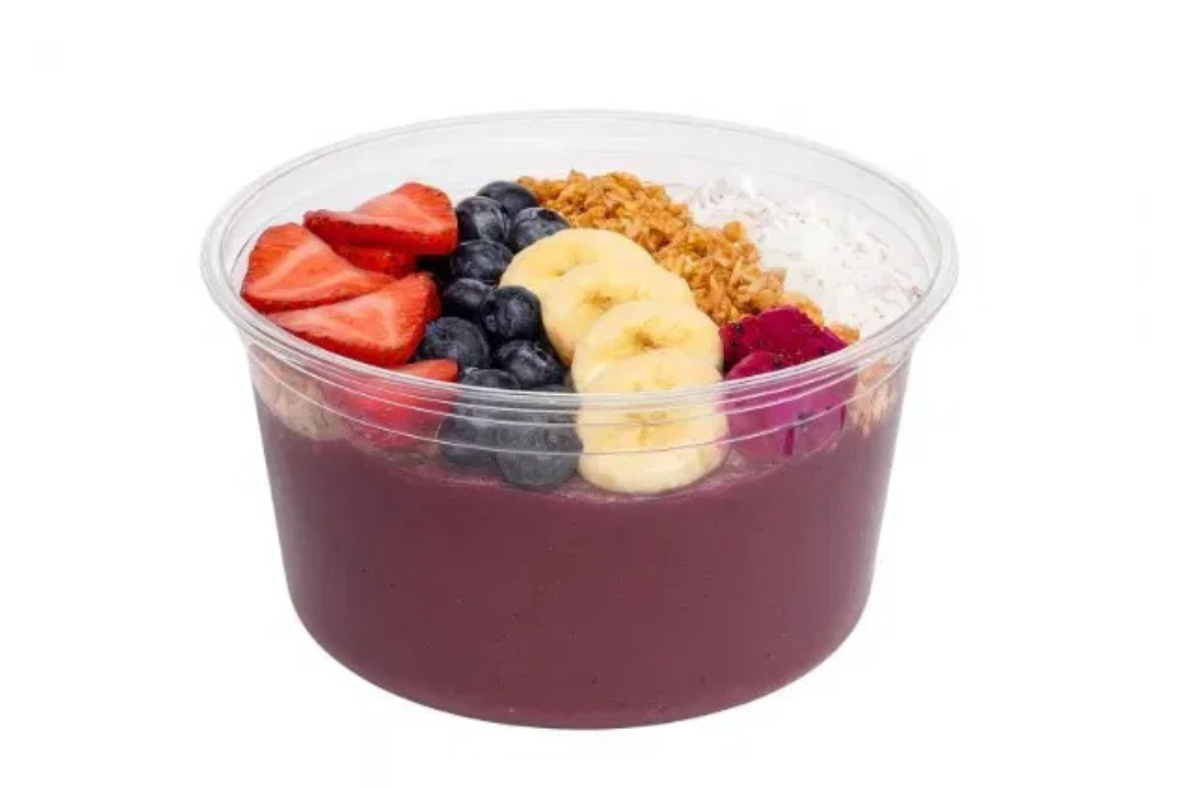 Acai bowl with strawberries, blueberries, banana slices, and granola in a clear plastic container.