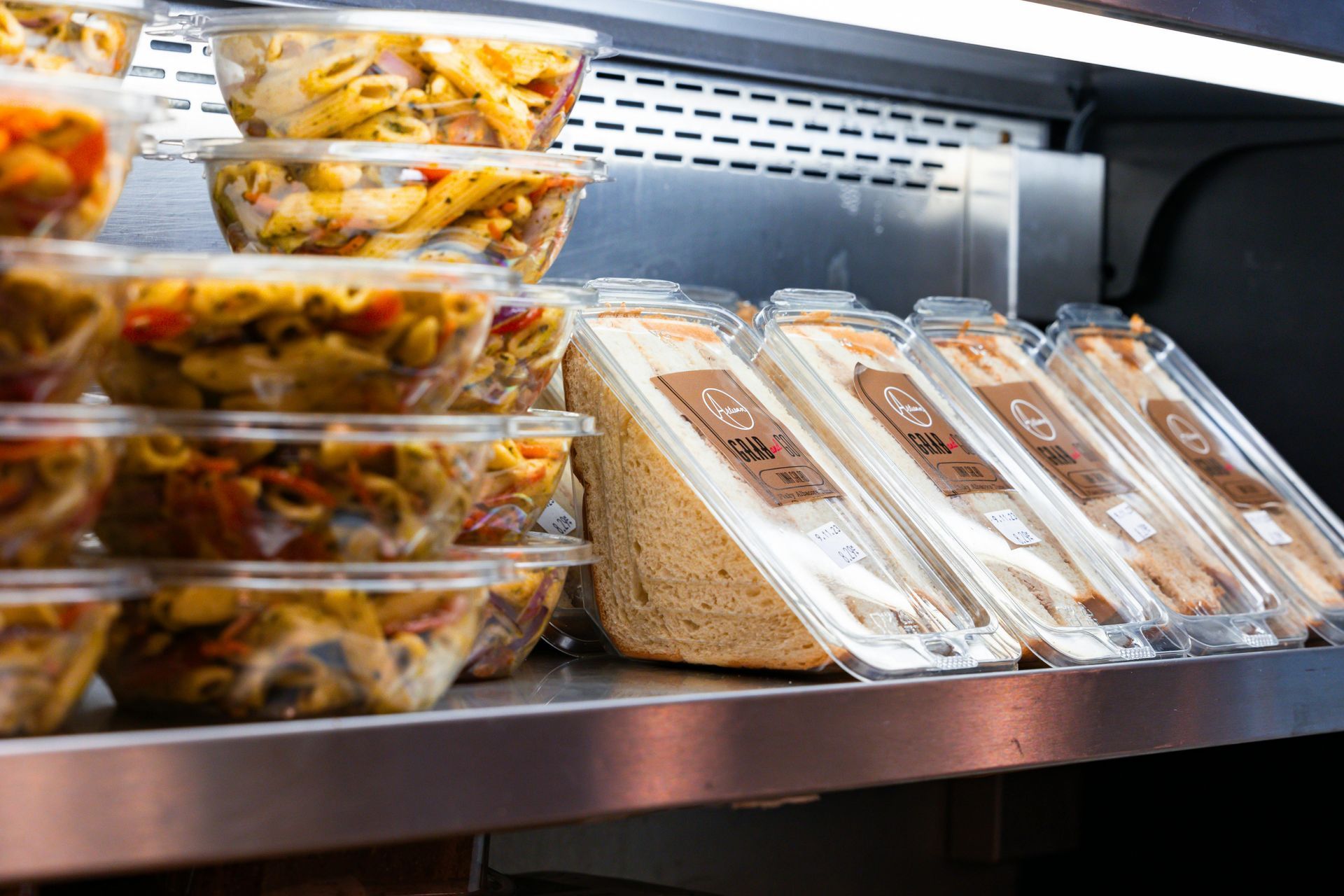 Prepared pasta and sandwiches in plastic containers on a shelf, ready for sale.