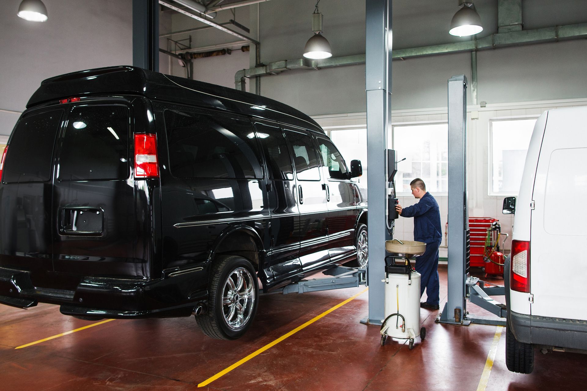 A mechanic works on a lifted black van inside an automotive repair shop.