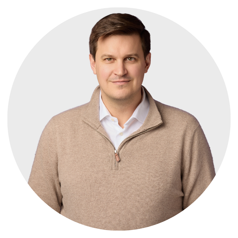 Portrait of a man in a tan sweater and white shirt against a light gray background