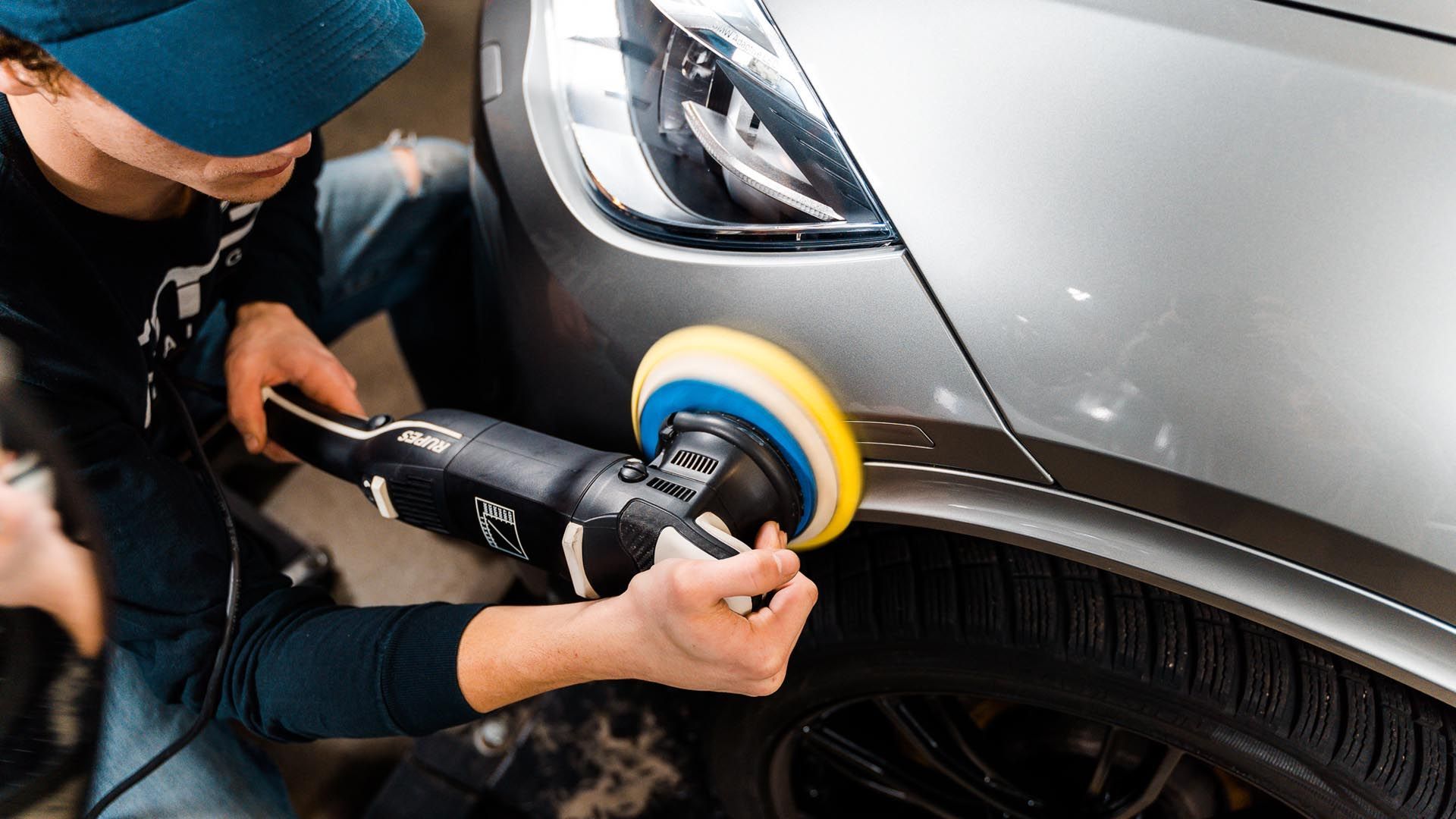 Person polishing a gray car with a power buffer.