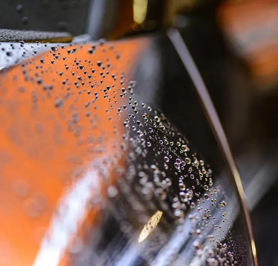 Water droplets on a curved glass surface, reflecting orange and black details.