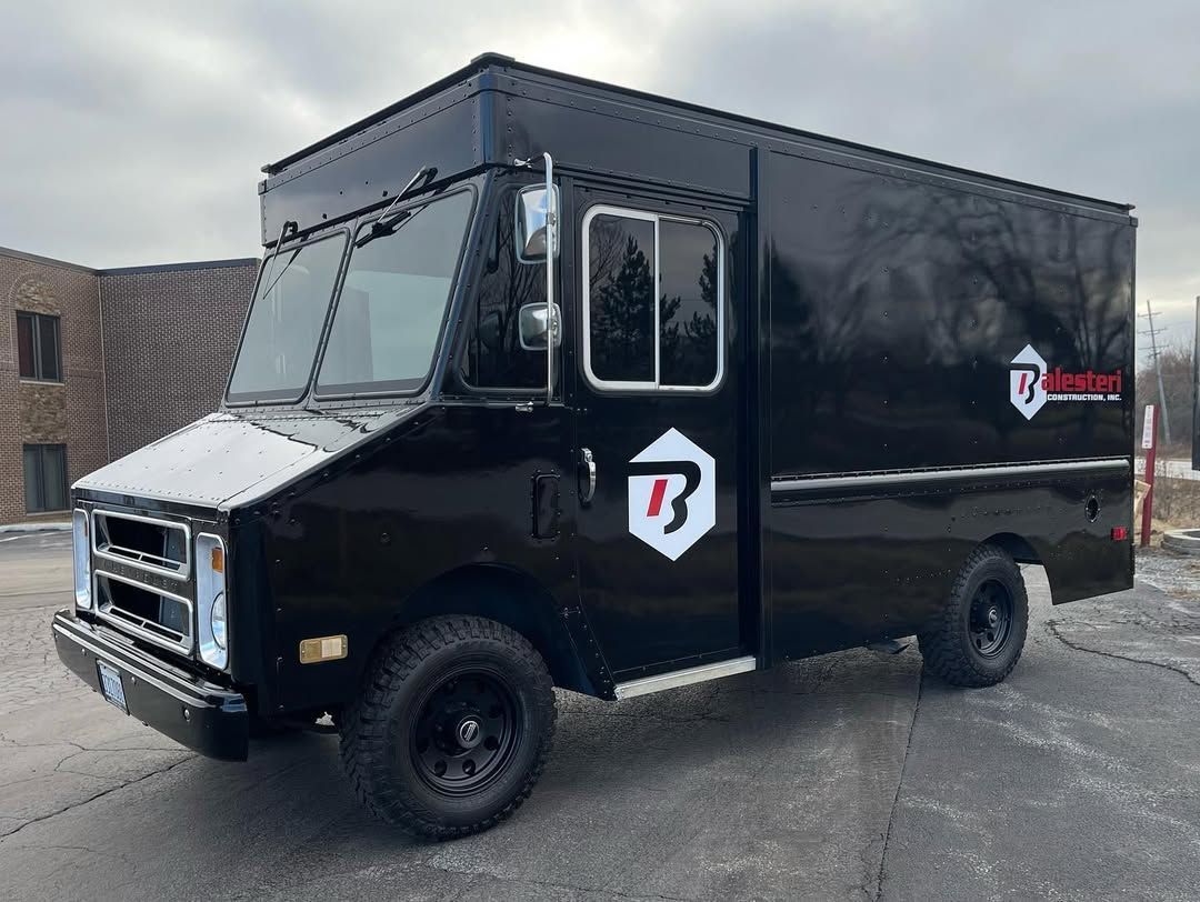 Black delivery truck with logo on the side, parked on asphalt.