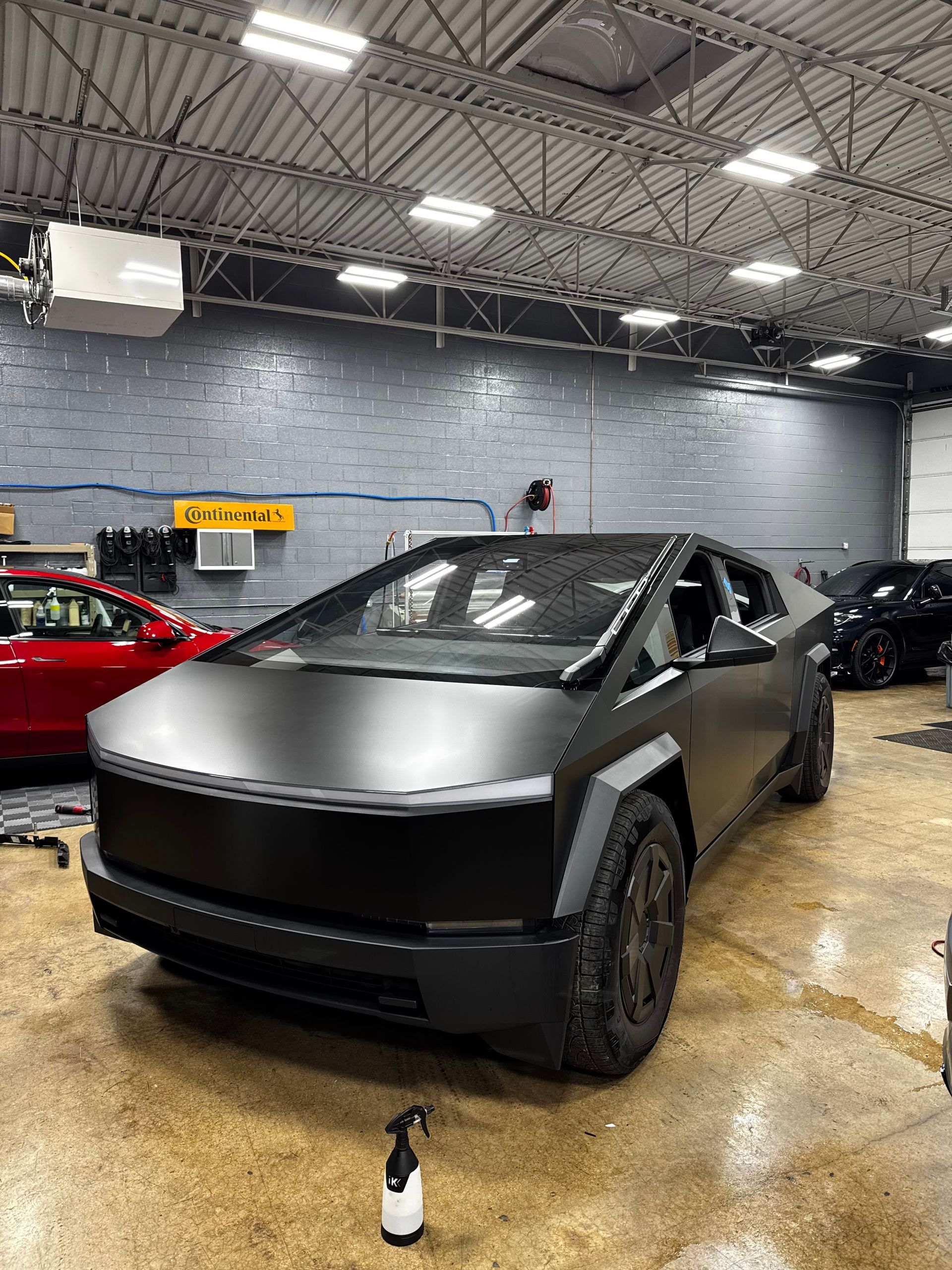 Matte black Tesla Cybertruck in a garage, with another car partially visible.
