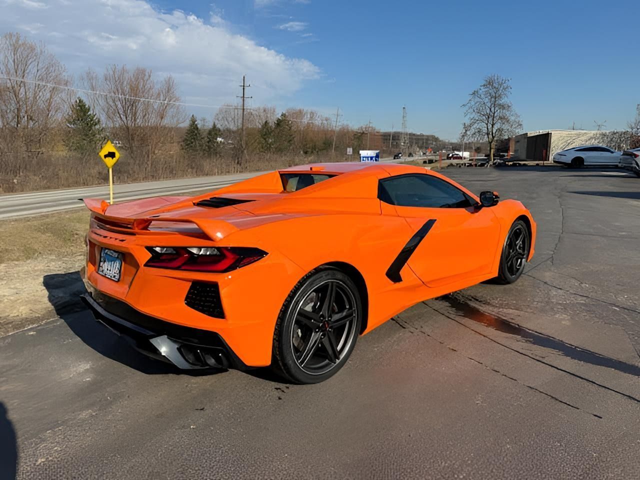 Orange sports car parked in a lot, with black wheels and a spoiler.