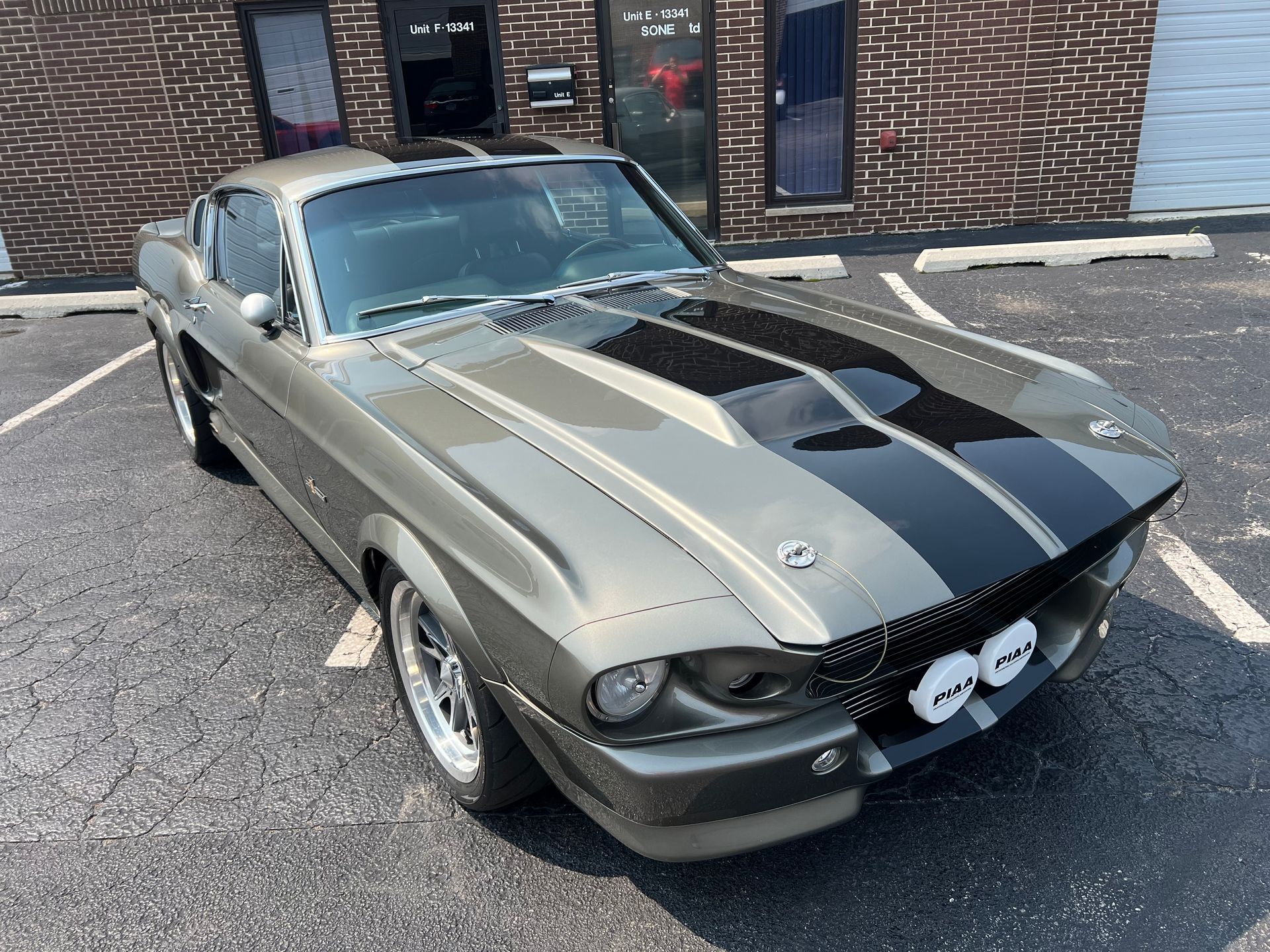Gray and black classic Mustang with black racing stripes parked outside a building.