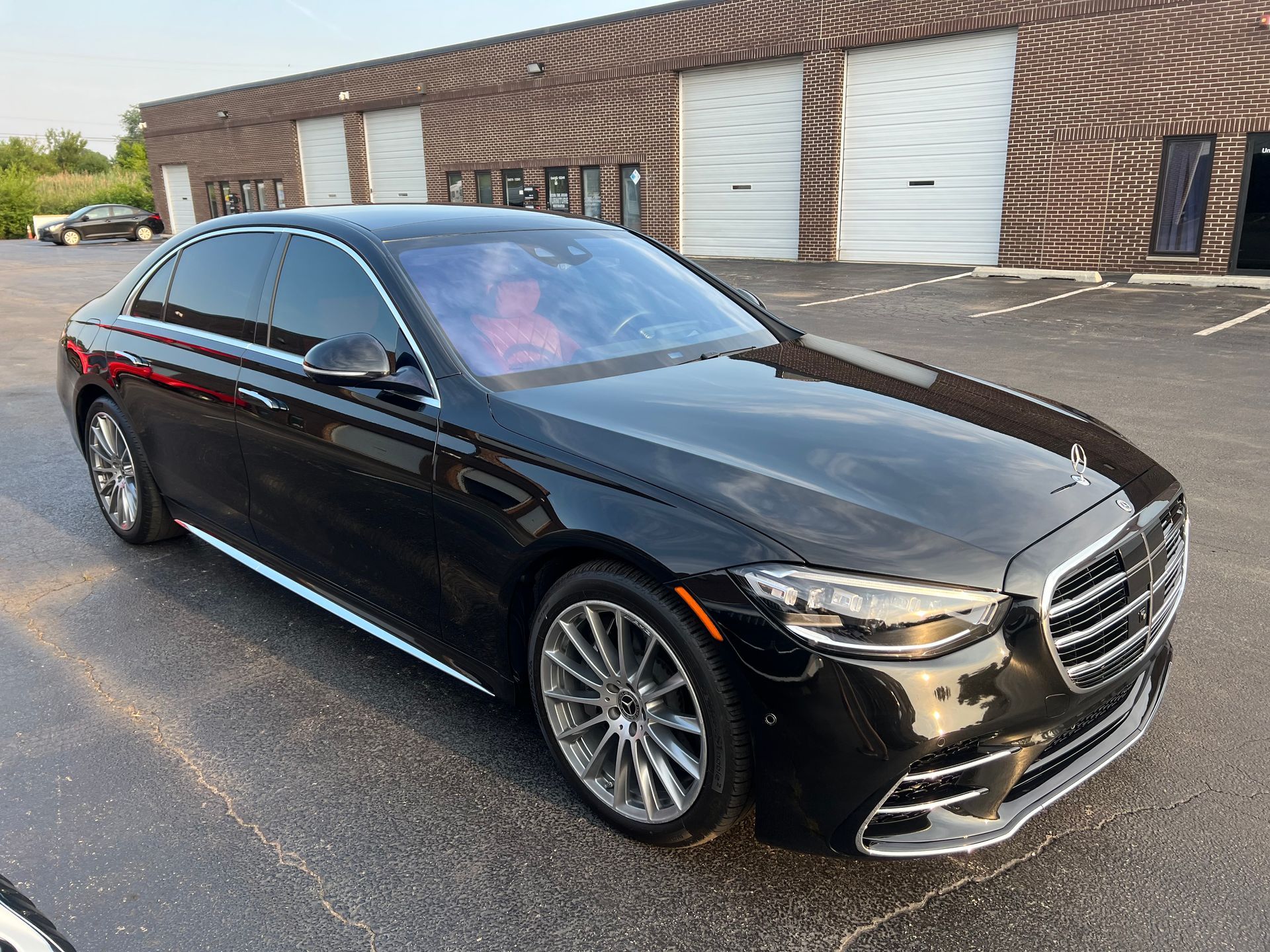 Black Mercedes-Benz sedan parked in front of a brick building with white garage doors, reflecting sunlight.