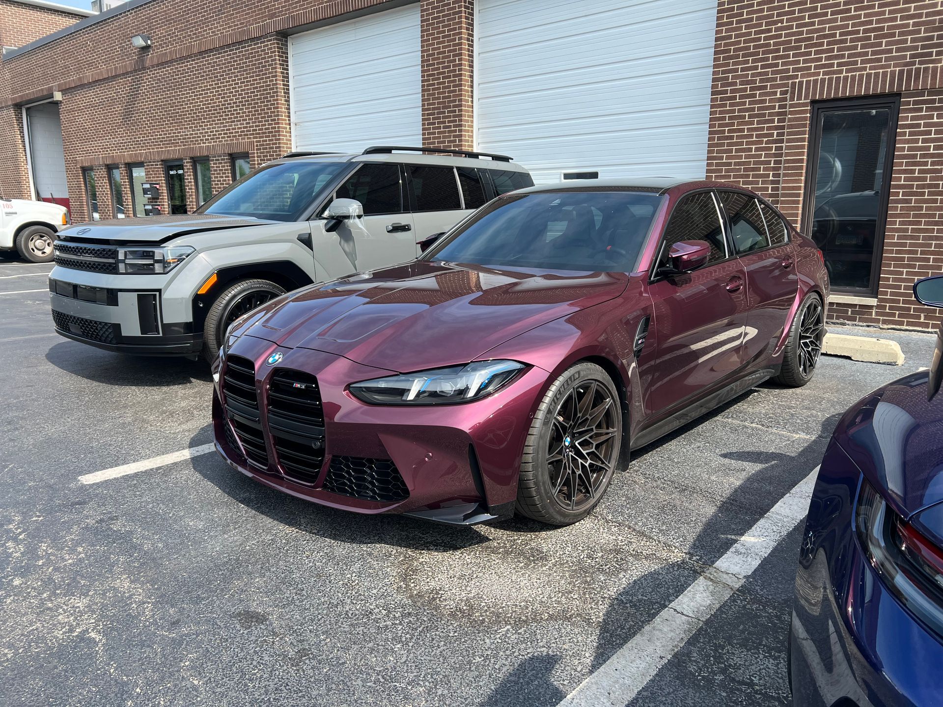 A burgundy BMW M3 parked in front of a gray SUV, both in a parking lot.