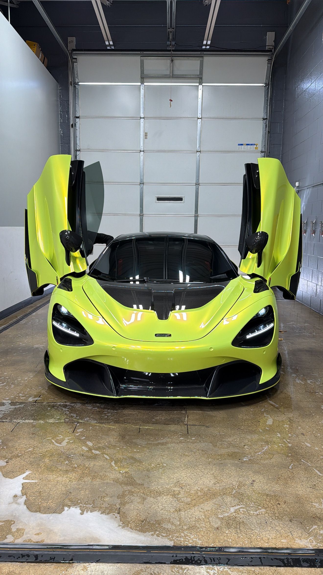 Lime green McLaren sports car with doors open, in a garage.