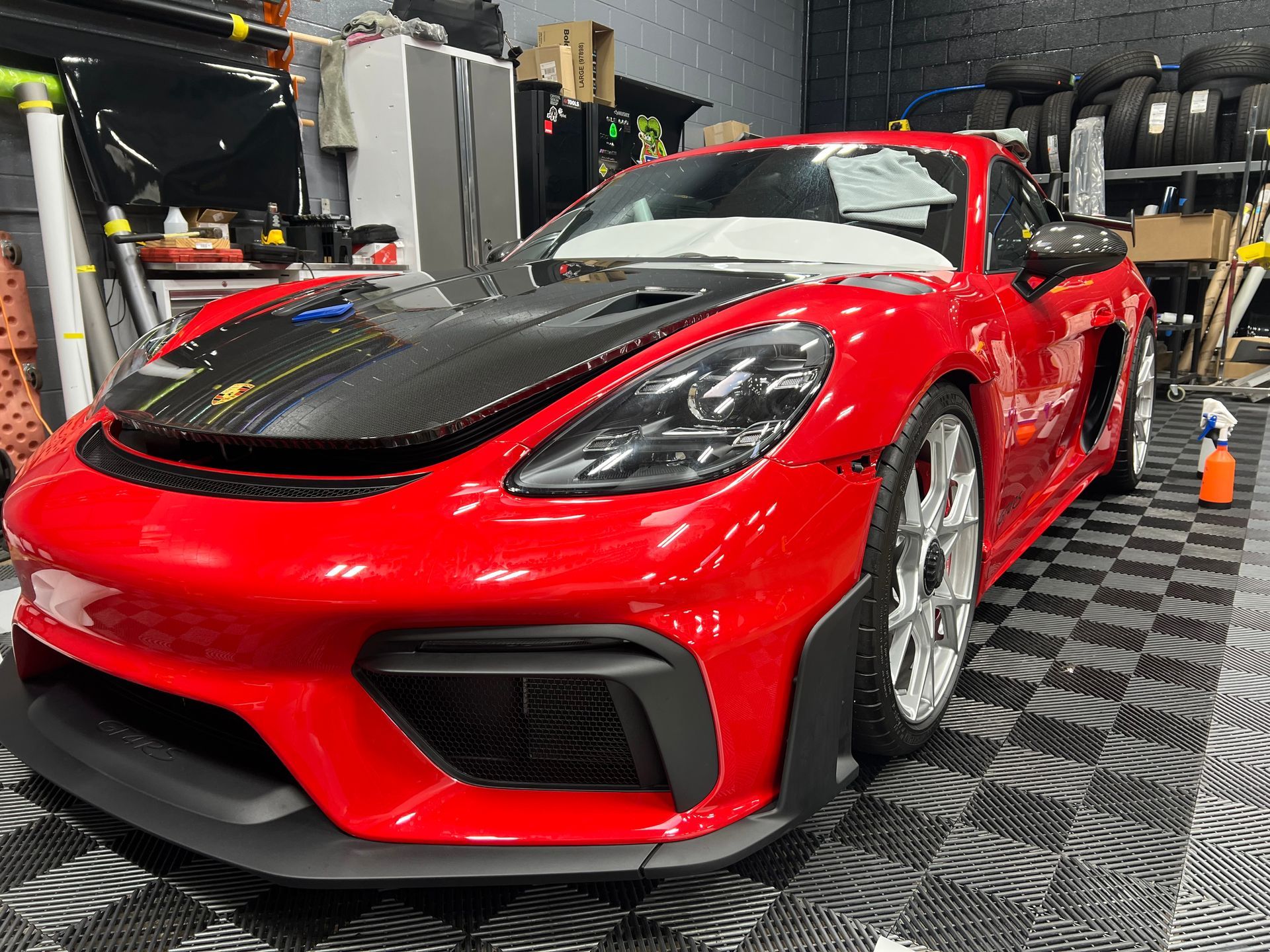 Red Porsche sports car with carbon fiber hood in a garage.