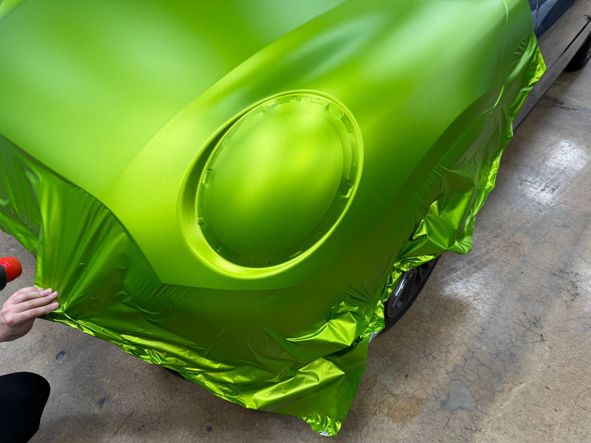 Blue BMW M4 coupe in a garage, black roof, matte finish. Black wheels, tires, equipment visible.