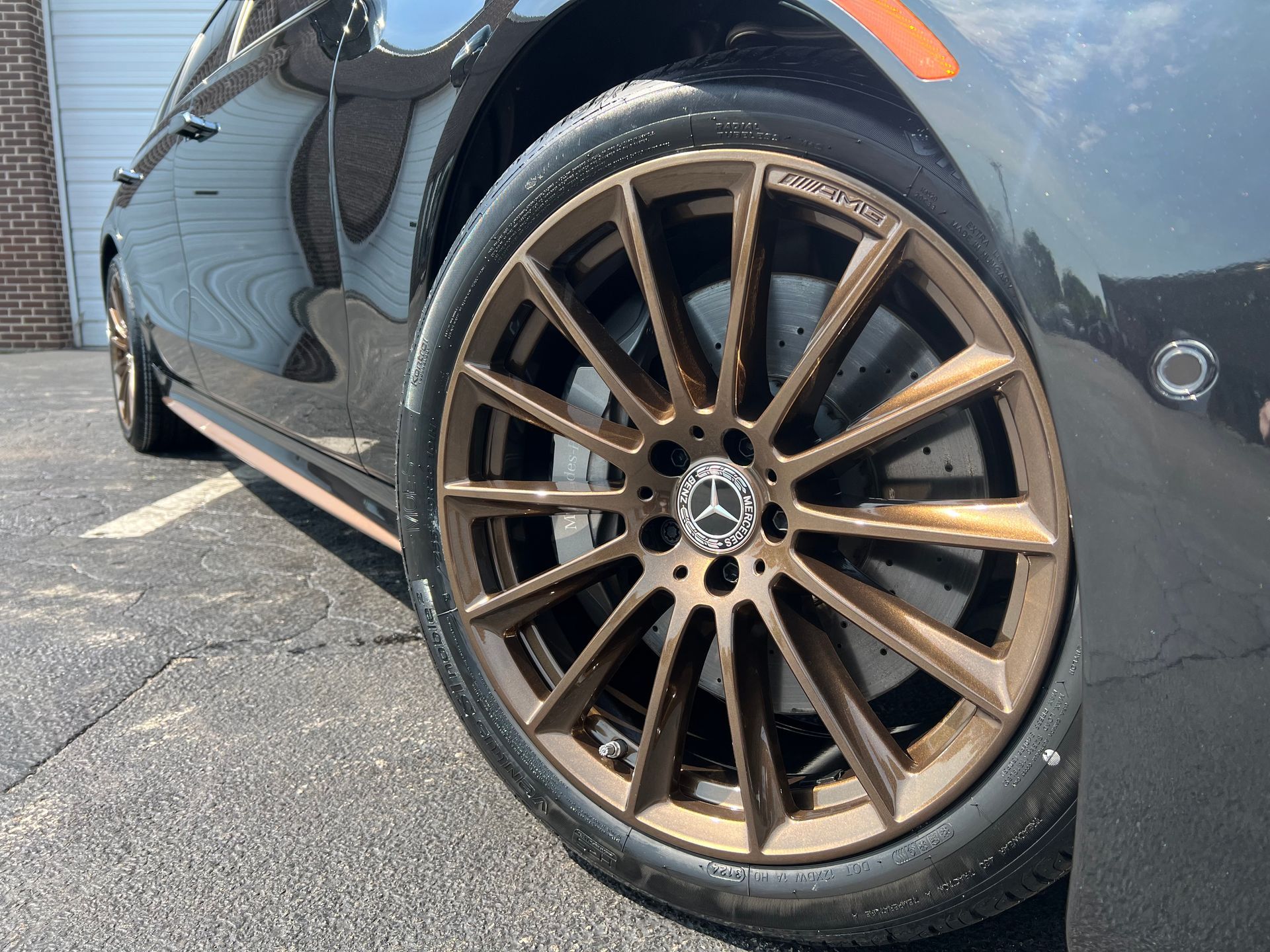 Bronze alloy wheel on a black Mercedes sedan parked outside.