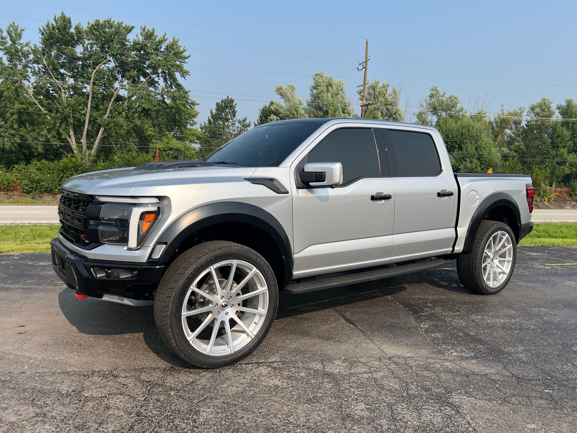 Silver Ford F-150 Raptor pickup truck with custom wheels, parked outside on a sunny day.