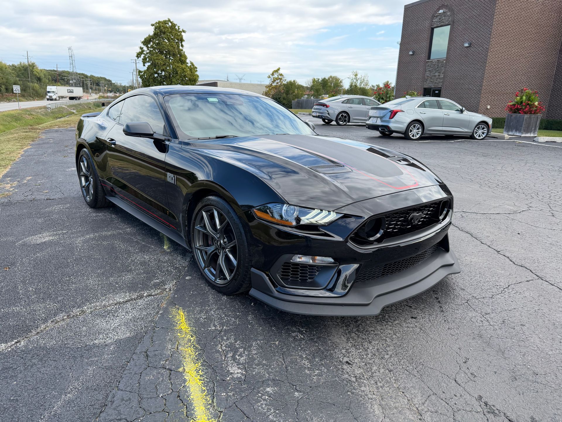 Black Ford Mustang coupe parked on asphalt, front view. Building and other cars in the background.