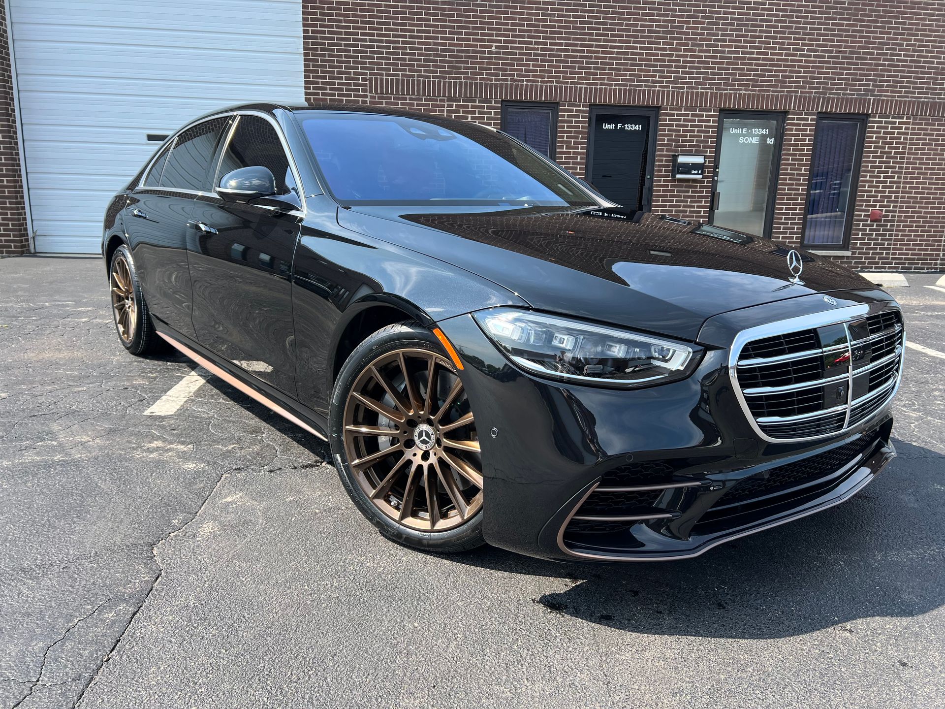 Black Mercedes-Benz sedan with bronze wheels parked in front of a brick building.