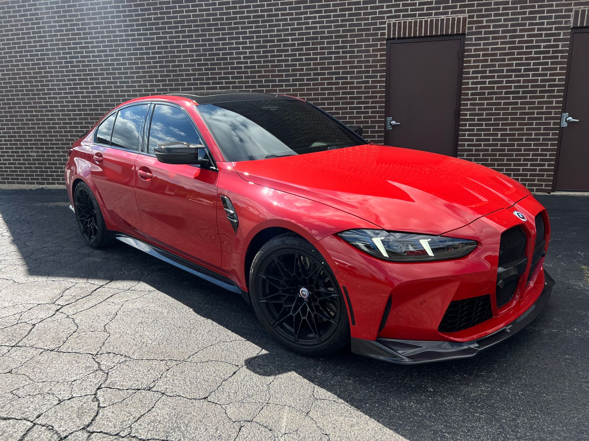 Red BMW M3 parked in front of a brick building. Black rims and a carbon fiber front splitter.