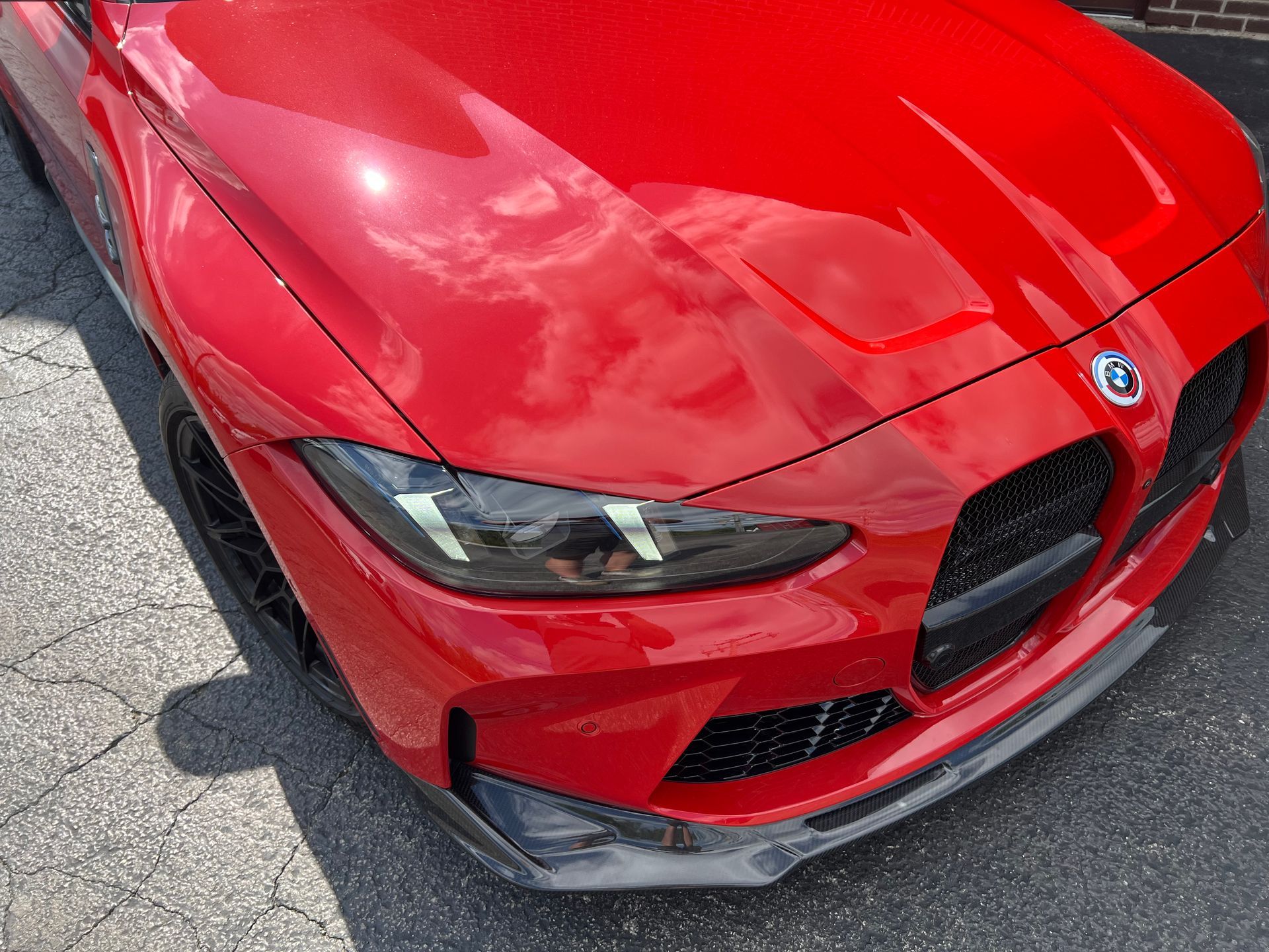 Red BMW car hood, reflecting a sky with clouds.