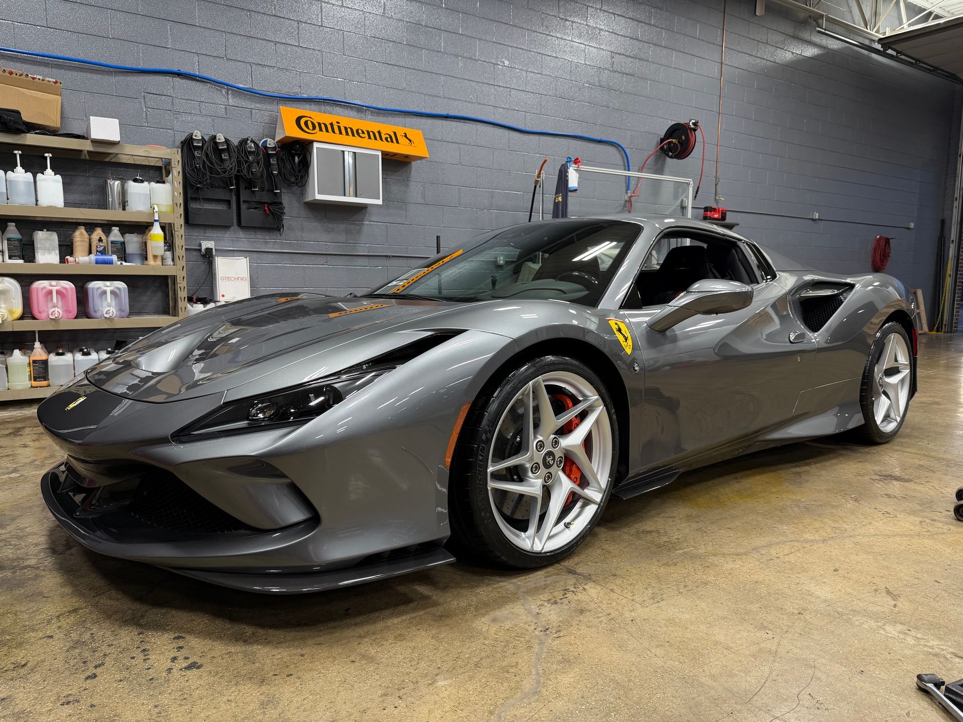 A gray Ferrari sports car with red brake calipers in a garage.