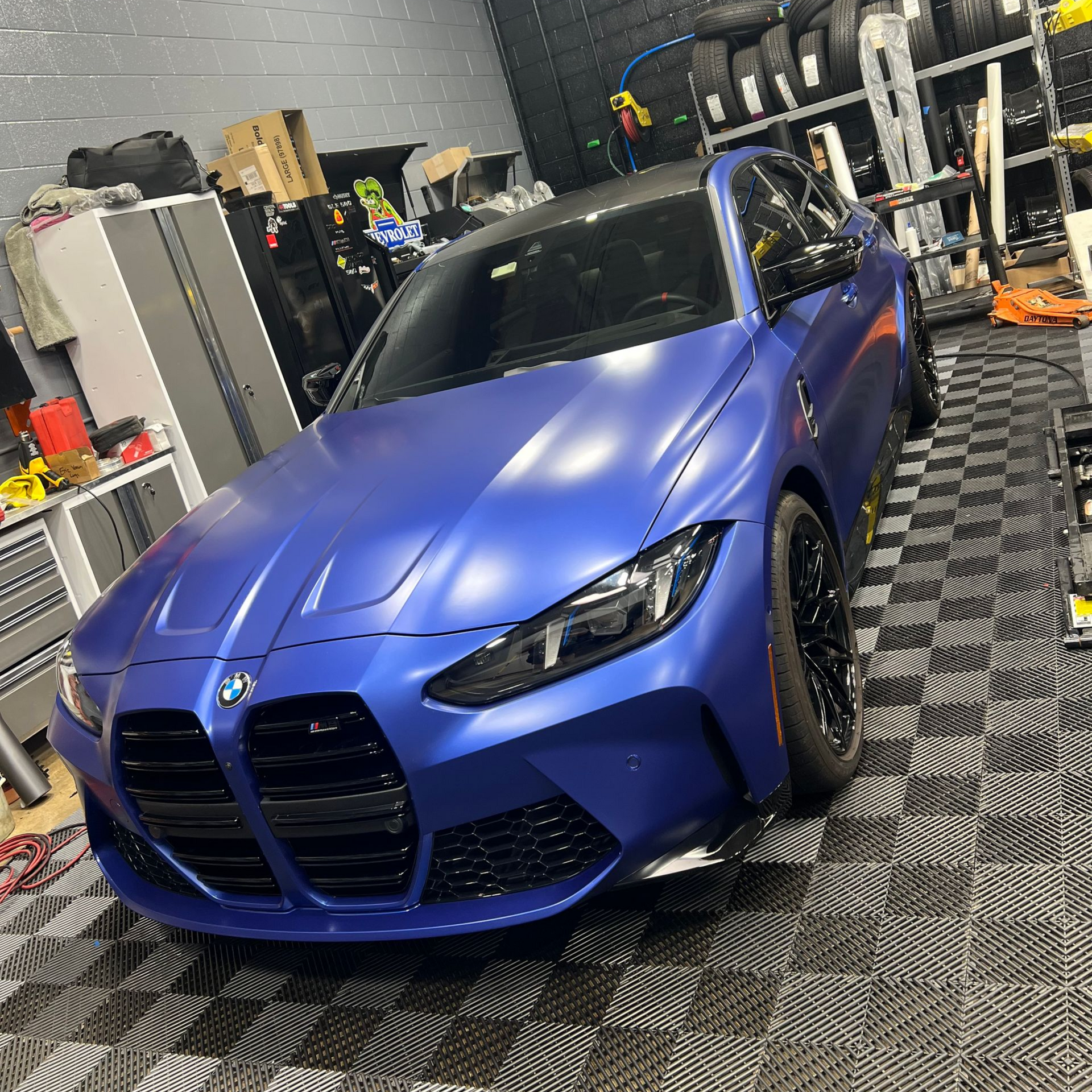 Blue BMW M4 car parked in a garage with black trim, black wheels, and a black roof.