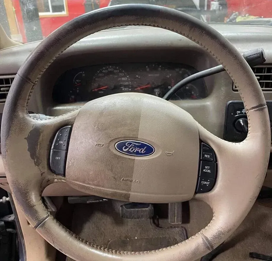 Steering wheel showing before and after cleaning, Ford logo, tan color, dashboard in the background.