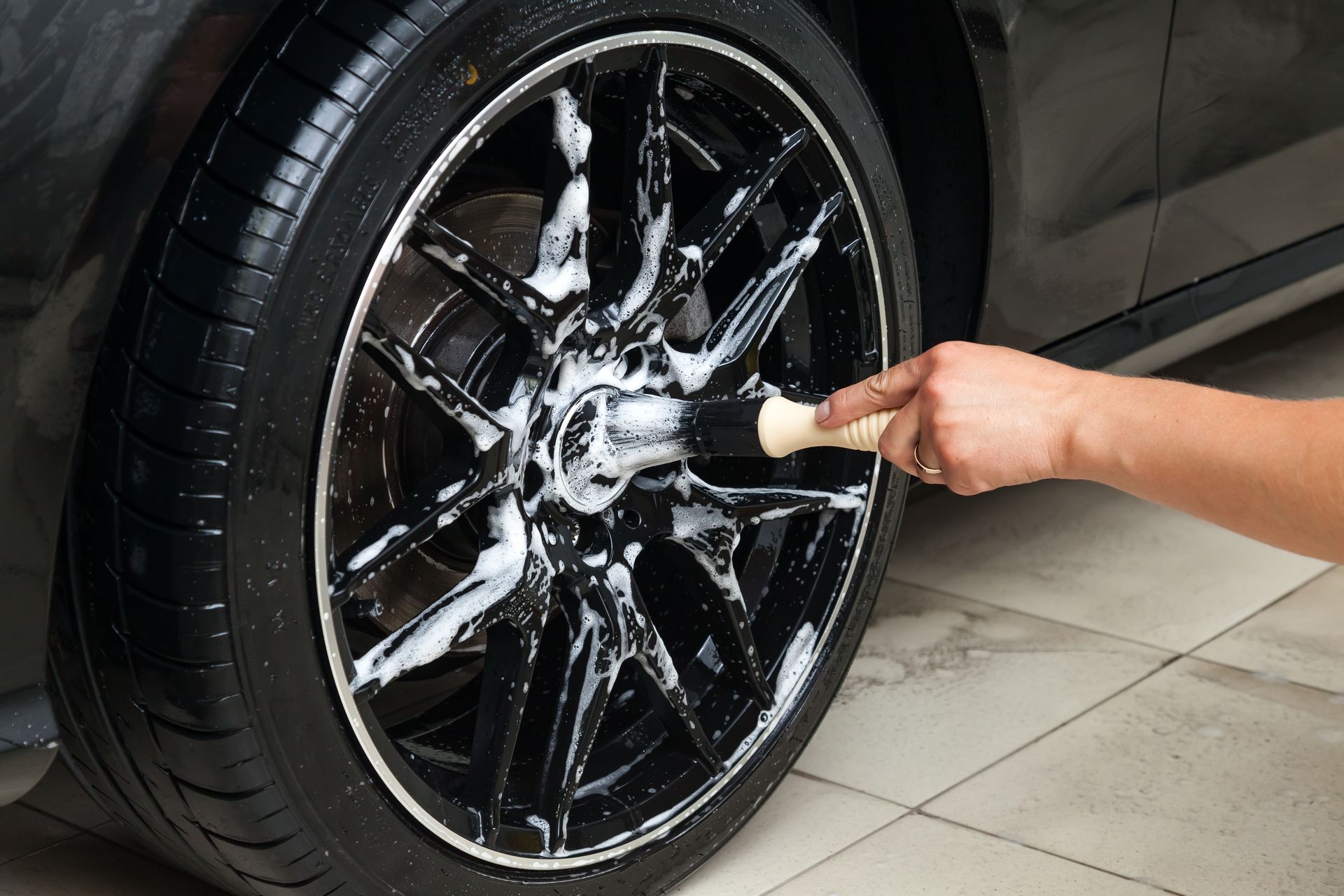 Hand scrubbing a black car rim with soapy water and a brush.