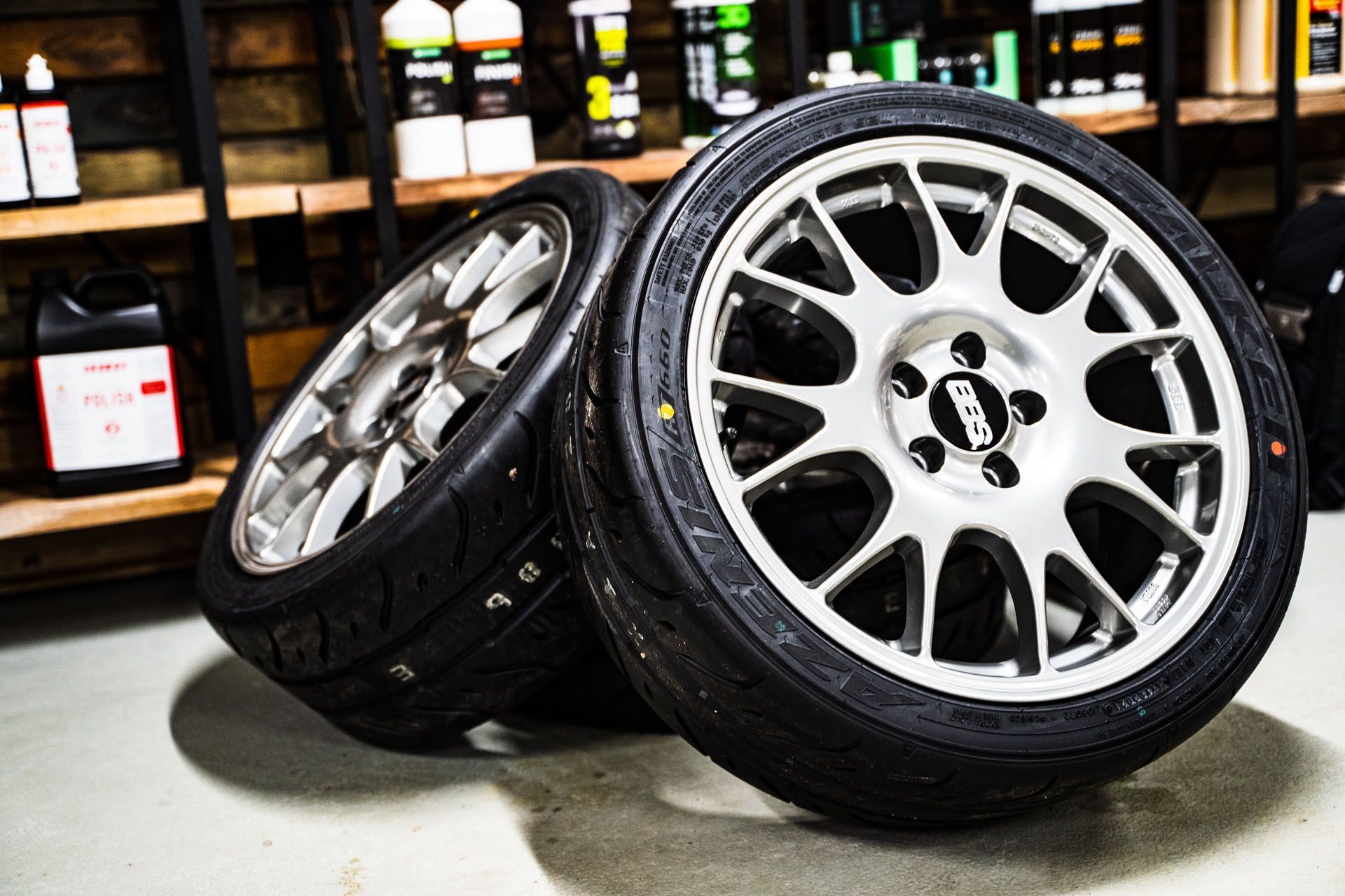 Two silver BBS wheels with black tires in a shop.