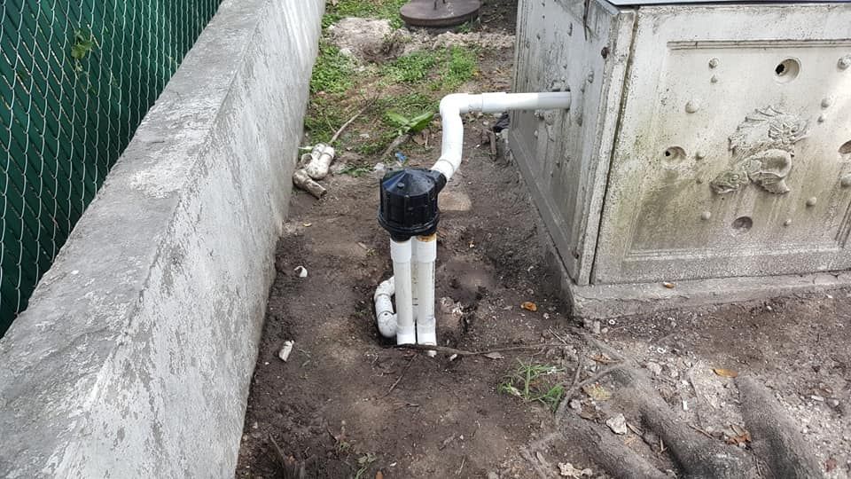 A white pipe is sitting in the dirt next to a concrete wall.