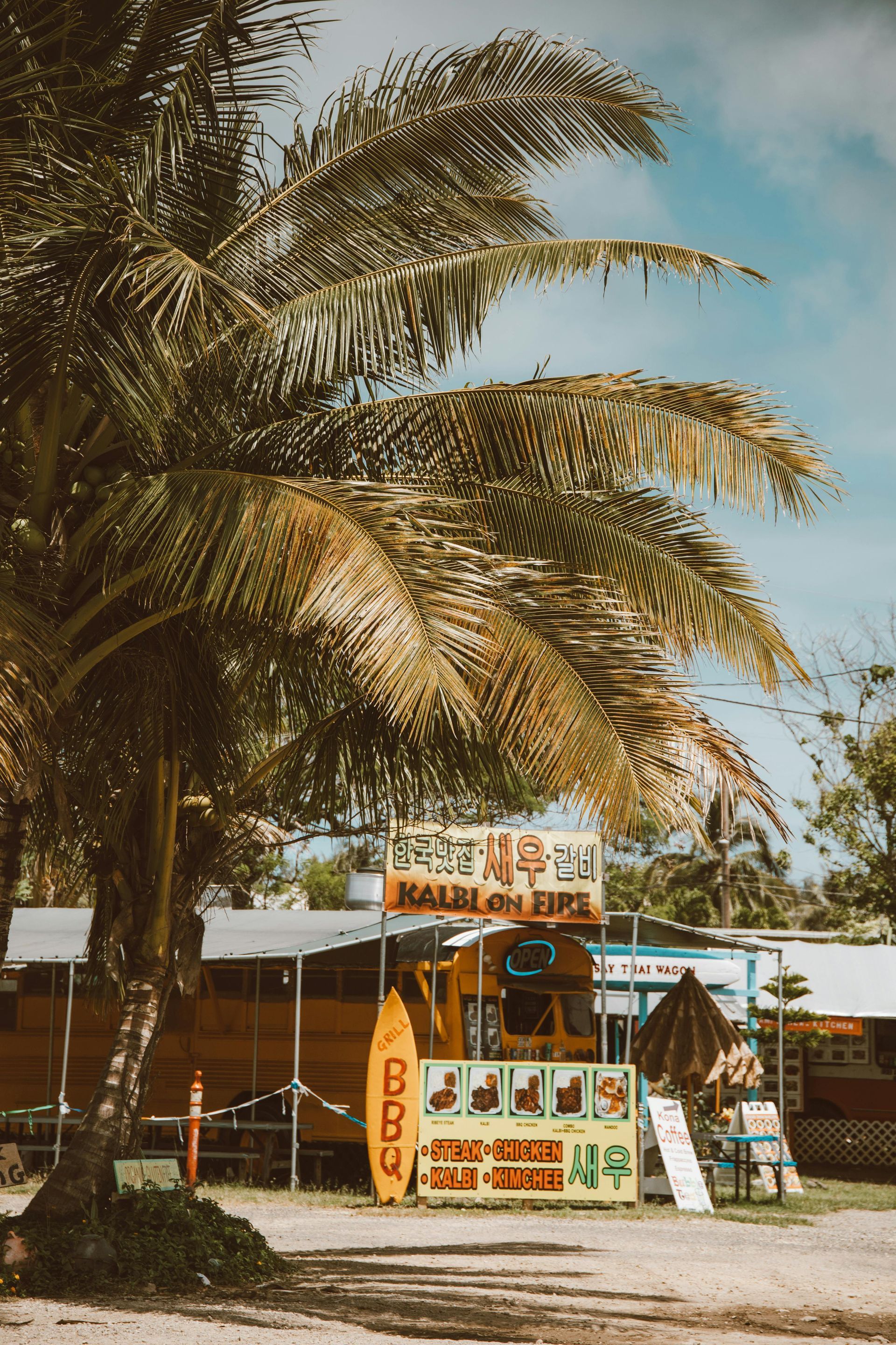A surfboard is sitting in front of a food truck on the beach.