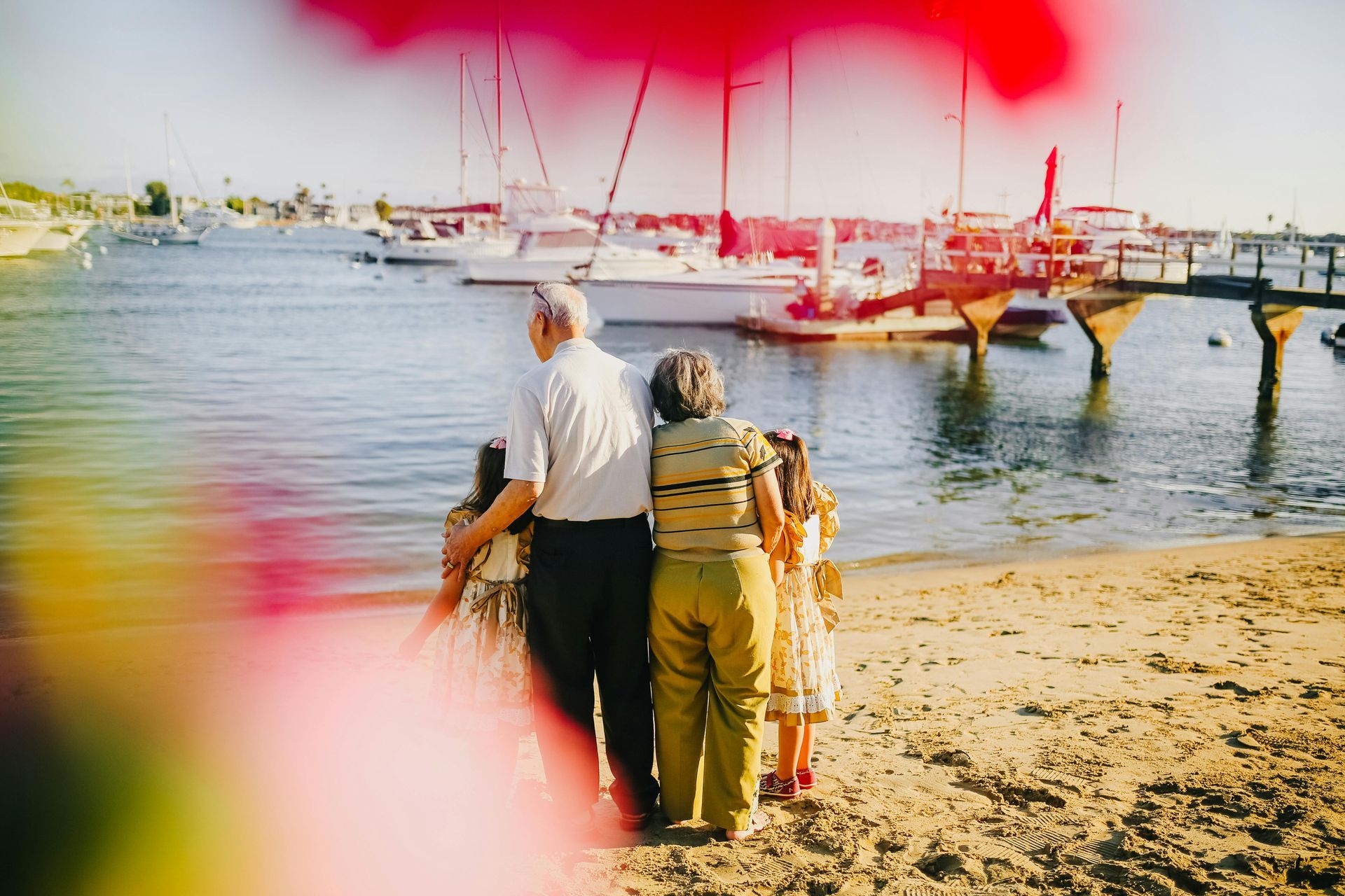A group of people from different generations are standing on a beach looking at the water.
