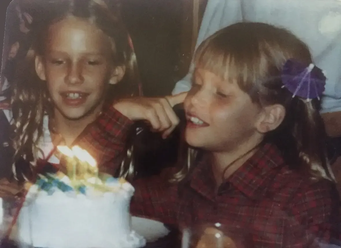 7 year old Loren blowing out the candles on her birthday cake while Paula sits next to her.