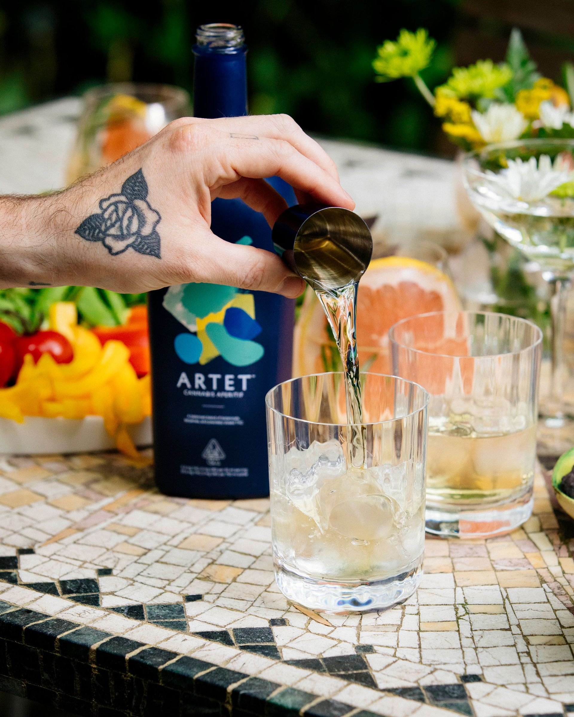 A hand pouring a shot of ARTET aperitif into a glass with ice to make a THC mocktail