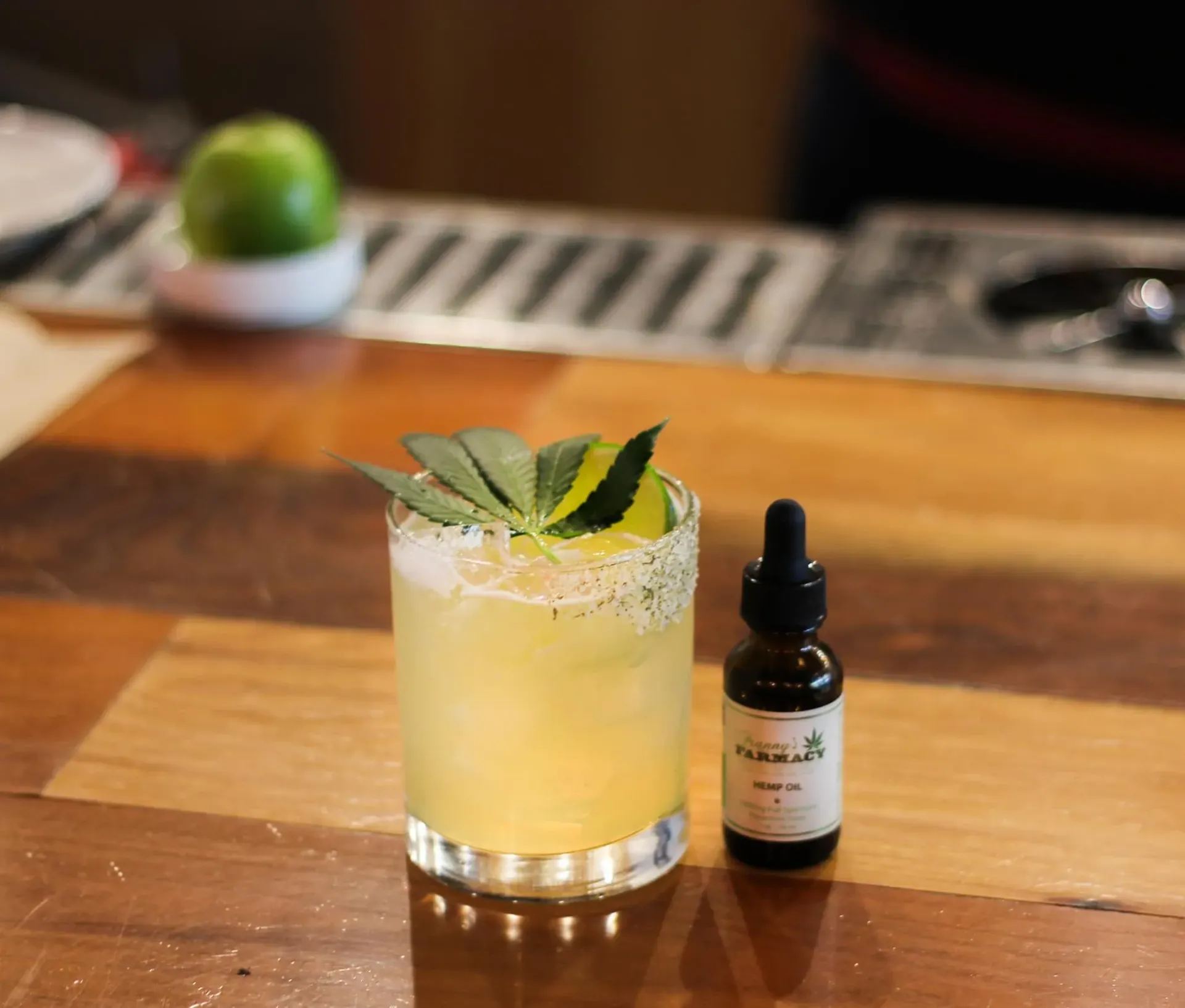 Cocktail with lime garnish, salt rim, and CBD oil bottle on a wooden bar top.