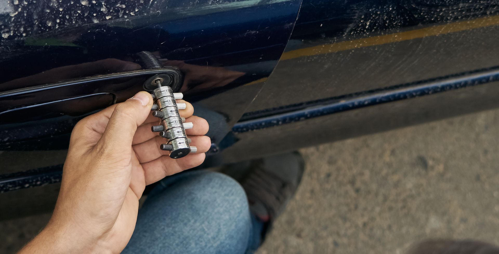 Hand holding a small metal car door handle latch near a dark blue vehicle door